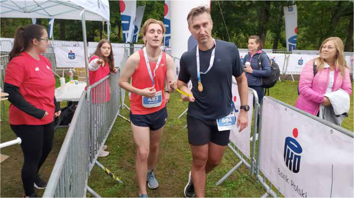 Zawodnik z przewodnikiem opuszczają trasę biegu za linią mety z wręczonymi im medalami.