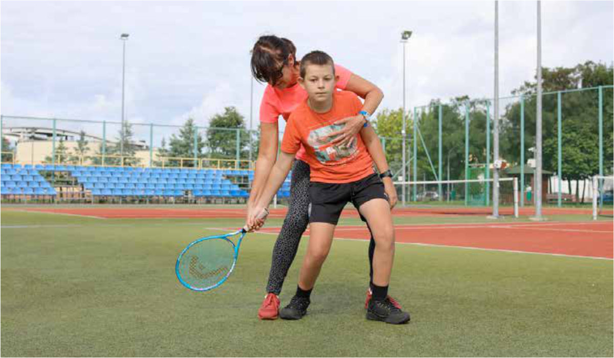 Trenerka Dorota Nowak instruuje chłopca Jakuba Palucha jak brać zamach rakietą tenisową.