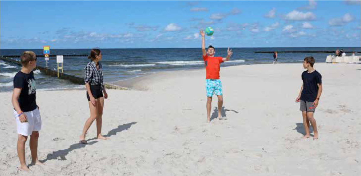 Młodzież korzysta z pogody na plaży bawiąc się piłką.