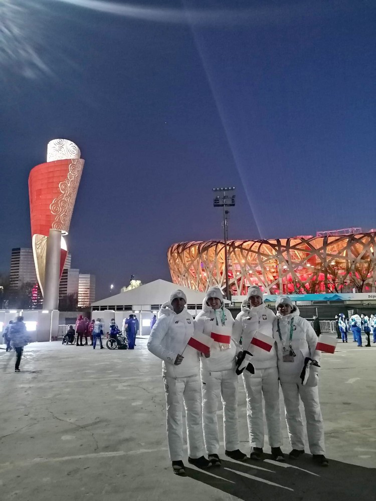 Cztery osoby w białych strojach na tle stadionu