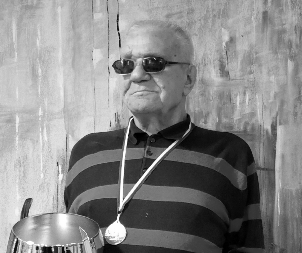 czarno-białe zdjęcie na kt&oacute;rym jest mężczyzna z pucharem w ręku i medalem na szyi