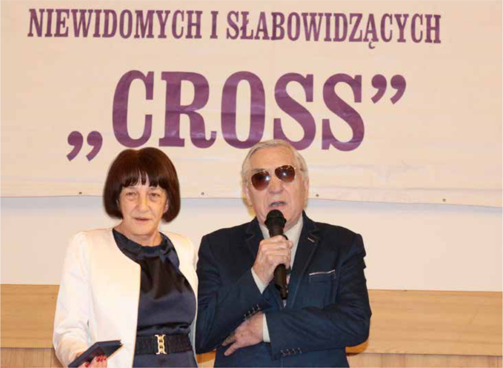 Mężczyzna przemawia z mikrofonem, obok stoi kobieta