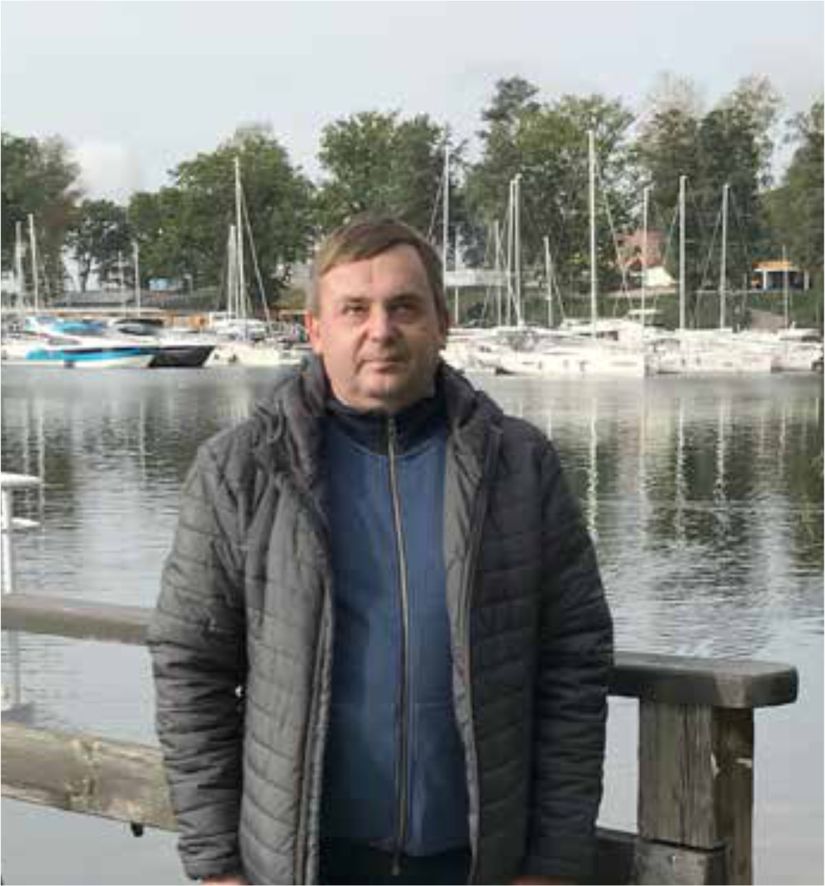 Andrzej Gasiul pozuje do zdjęcia na tle portu jachtowego.