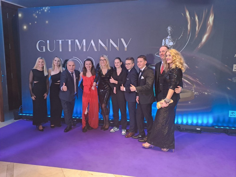 grupa osób na tle napisu gutmanny